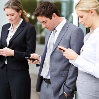 Group of four male and female executives using their cellphones outside their office