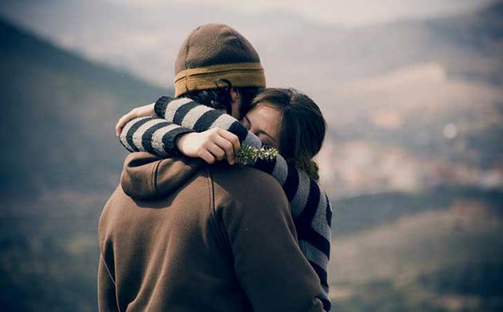 par-de-amigos-abrazados-el-sudadera-y-gorro-cafe-ella-sueter-rayado-flor-en-la-mano