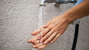 woman washing hands under faucet against wall