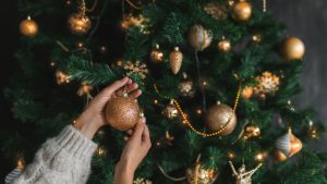 Woman putting on christmas tree golden ornaments.
