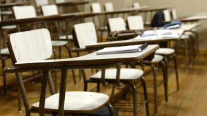 desks in a classroom with notebooks and pens, with no people occupying the seats.