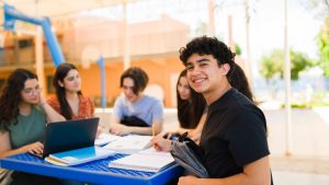 Happy high school student studying with friends in schoolyard