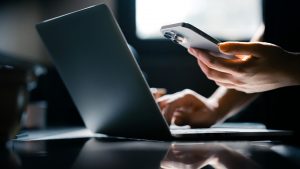 Close-up shot of a woman using mobile device with Two-Factor Authentication (2FA) security while logging in securely to her laptop. Privacy protection, internet and mobile security