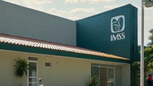 Exterior view of an IMSS Unidad de Medicina Familiar (UMF) in Mexico, featuring the institution's logo on the green and beige facade with a tiled roof.