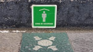 Spanish-language sign stating 'Zona de seguridad' [Safety Zone] and evacuation assembly point sign painted on a paving stone