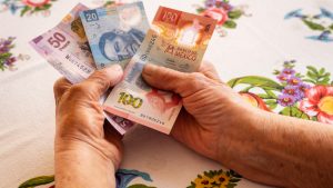 Mexican money, a pensioner holds several pesos banknotes in her hand, Financial problems of seniors, low pensions in Mexico