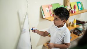 Student writing on a whiteboard in classroom at school