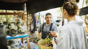Medium shot woman purchasing produce from vendor at farmers market