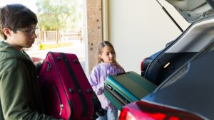 Teens and siblings packing suitcase in car trunk for family road trip or summer vacation travel