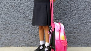 Latina brunette girl walks to class with her backpack dressed in uniform this back to school