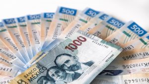 Macro close-up of stack of 1000 mexican pesos banknotes on fan of 500 pesos banknotes against white background