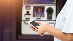 business Automatic Teller Machine concept, Close Up woman using the smart mobile phone for withdrawing the cash in front of the ATM