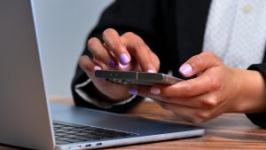 Close-up of a businesswoman's hands using a smartphone on a laptop